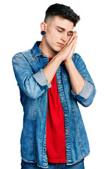 Young caucasian boy with ears dilation wearing casual denim jacket sleeping tired dreaming and posing with hands together while smiling with closed eyes.