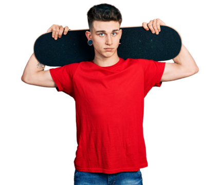 Young caucasian boy with ears dilation holding skate over shoulders relaxed with serious expression on face. simple and natural looking at the camera.