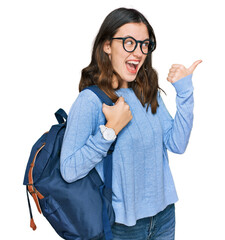 Young beautiful girl wearing student backpack pointing thumb up to the side smiling happy with open...