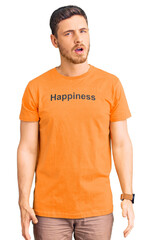 Fototapeta premium Handsome young man with bear wearing tshirt with happiness word message in shock face, looking skeptical and sarcastic, surprised with open mouth