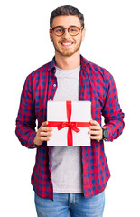 Handsome young man with bear holding gift looking positive and happy standing and smiling with a confident smile showing teeth