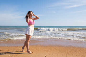 Fototapeta na wymiar Beautiful brunette girl on the sandy seashore in headphones listens to music