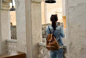  A young woman traveler with a backpack on her back walks and photographs the old narrow streets of Dubai Deira and Creek. Travel and sightseeing concept. © Ekaterina