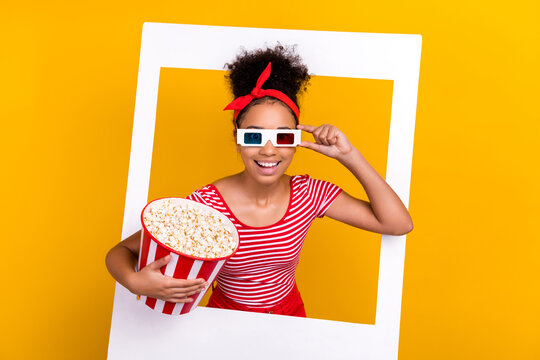 Portrait of excited funky teen girl hand touch 3d glasses hold popcorn box album set card moment isolated on yellow color background