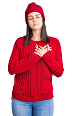 Young beautiful girl wearing sweater and wool cap smiling with hands on chest with closed eyes and grateful gesture on face. health concept.