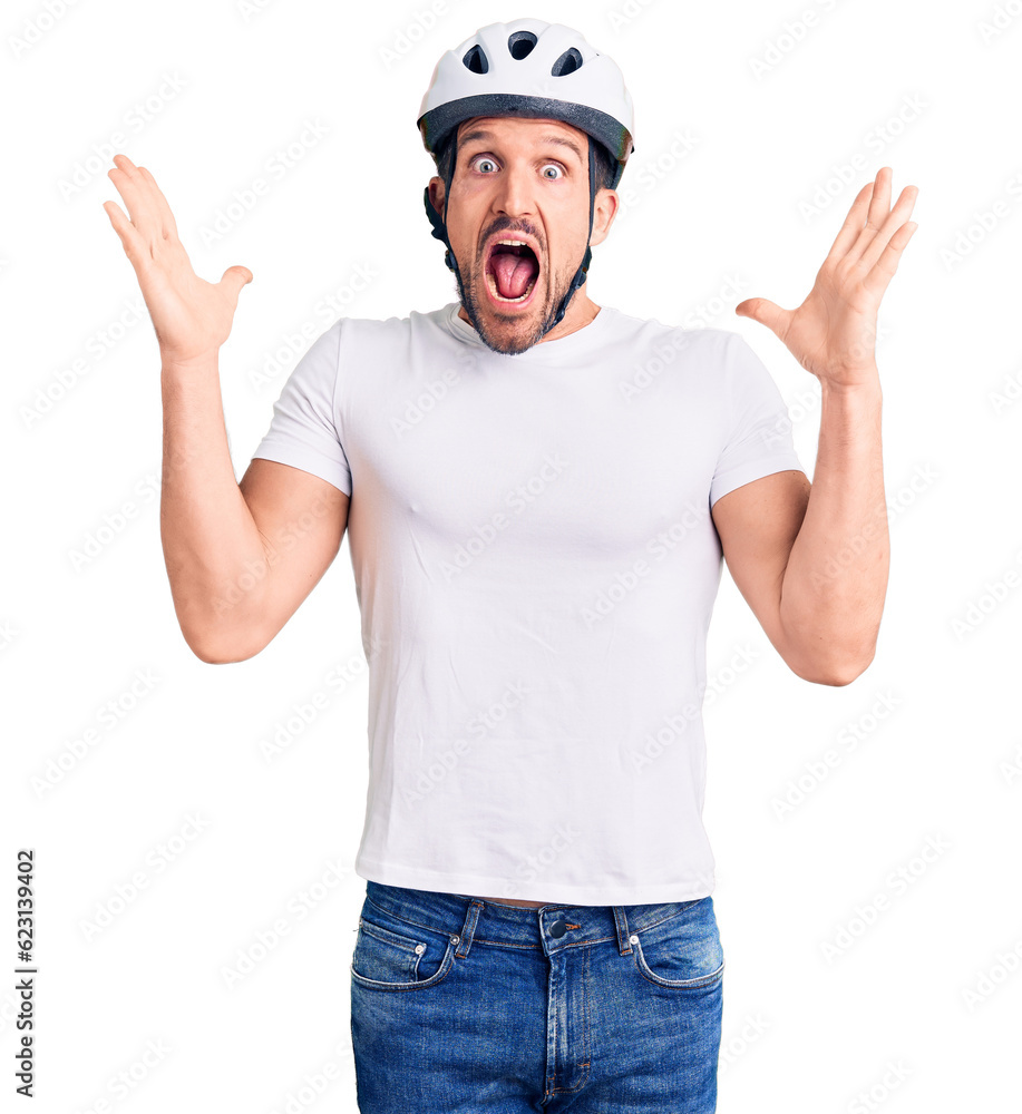 Wall mural Young handsome man wearing bike helmet celebrating crazy and amazed for success with arms raised and open eyes screaming excited. winner concept