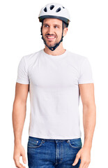 Young handsome man wearing bike helmet looking away to side with smile on face, natural expression. laughing confident.