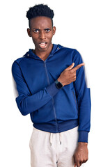 Young african american man wearing sportswear pointing aside worried and nervous with forefinger,...