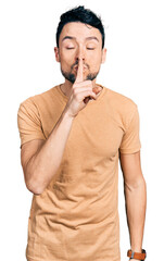 Hispanic man with beard wearing casual t shirt asking to be quiet with finger on lips. silence and secret concept.
