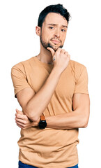 Hispanic man with beard wearing casual t shirt with hand on chin thinking about question, pensive expression. smiling with thoughtful face. doubt concept.