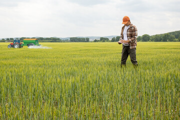 Farmer to use check list for check quality of agricultural work and  tractor spraying pesticides on a wheat field.