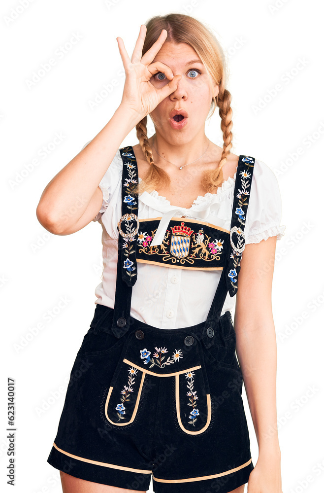 Wall mural Young beautiful blonde woman wearing oktoberfest dress doing ok gesture shocked with surprised face, eye looking through fingers. unbelieving expression.