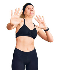 Fototapeta na wymiar Young beautiful blonde woman wearing sportswear afraid and terrified with fear expression stop gesture with hands, shouting in shock. panic concept.