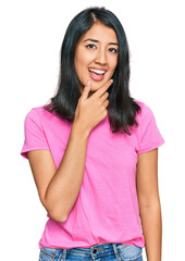 Fototapeta premium Beautiful asian young woman wearing casual pink t shirt looking confident at the camera smiling with crossed arms and hand raised on chin. thinking positive.