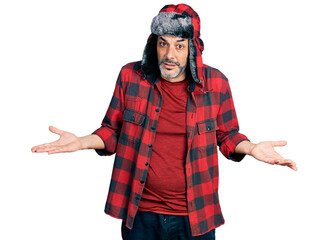 Middle age hispanic man with grey hair wearing fluffy earmuff hat clueless and confused expression...