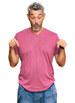 Middle age grey-haired man wearing casual clothes pointing down with fingers showing advertisement, surprised face and open mouth