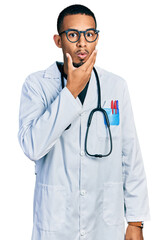 Fototapeta premium Young african american man wearing doctor uniform and stethoscope looking fascinated with disbelief, surprise and amazed expression with hands on chin