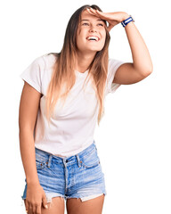 Beautiful caucasian woman wearing casual white tshirt very happy and smiling looking far away with hand over head. searching concept.