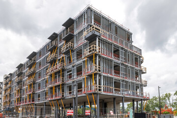 New housing starts mid-rise apartment building under construction, scaffolding, concrete floor slabs and steel studded exterior walls, daytime, cloudy, nobody