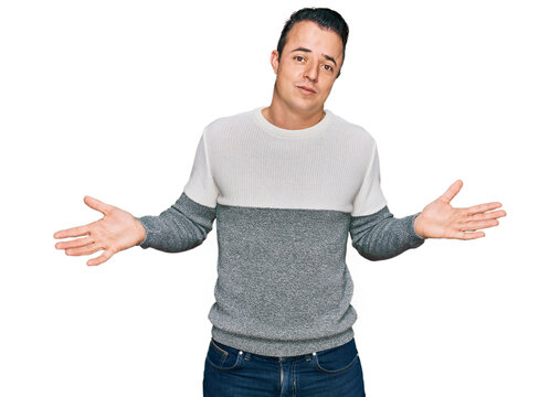 Handsome young man wearing casual winter sweater clueless and confused expression with arms and hands raised. doubt concept.