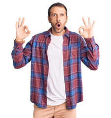 Naklejka premium Young handsome man wearing casual clothes looking surprised and shocked doing ok approval symbol with fingers. crazy expression