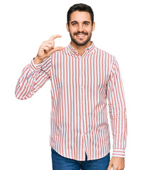 Young hispanic man wearing business shirt smiling and confident gesturing with hand doing small size sign with fingers looking and the camera. measure concept.