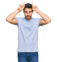 Young hispanic man wearing casual clothes doing funny gesture with finger over head as bull horns