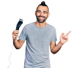 Hispanic man with ponytail holding electric razor machine smiling happy pointing with hand and finger to the side