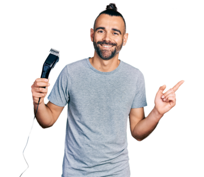Hispanic man with ponytail holding electric razor machine smiling happy pointing with hand and finger to the side
