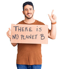 Young hispanic man holding there is no planet b banner surprised with an idea or question pointing finger with happy face, number one