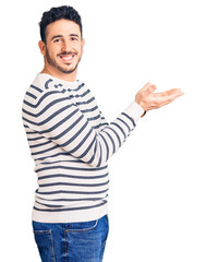 Fototapeta premium Young hispanic man wearing casual clothes pointing aside with hands open palms showing copy space, presenting advertisement smiling excited happy