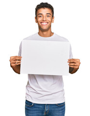 Young handsome african american man holding blank empty banner looking positive and happy standing and smiling with a confident smile showing teeth