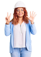 Young latin woman wearing architect hardhat showing and pointing up with fingers number seven while smiling confident and happy.