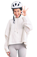Beautiful brunette young woman wearing bike helmet and sporty clothes smiling positive doing ok sign with hand and fingers. successful expression.