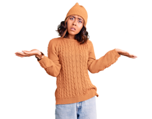 Young beautiful mixed race woman wearing wool sweater and winter hat clueless and confused with open arms, no idea concept.