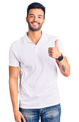 Young handsome hispanic man wearing casual clothes doing happy thumbs up gesture with hand. approving expression looking at the camera showing success.