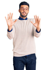 Naklejka premium Young handsome hispanic man wearing elegant clothes and glasses afraid and terrified with fear expression stop gesture with hands, shouting in shock. panic concept.