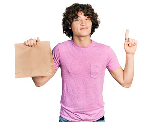 Caucasian teenager holding take away paper bag smiling with an idea or question pointing finger with happy face, number one