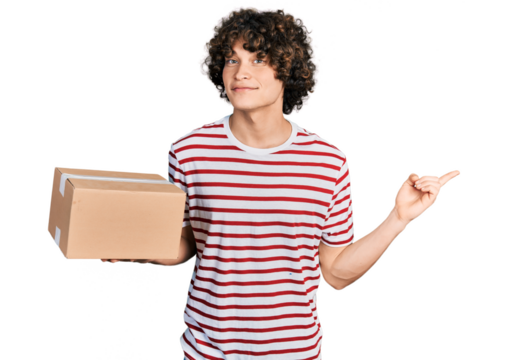 Caucasian teenager holding delivery package smiling happy pointing with hand and finger to the side