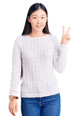 Young beautiful chinese woman wearing casual sweater smiling looking to the camera showing fingers doing victory sign. number two.