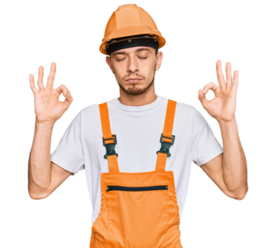 Hispanic young man wearing handyman uniform and safety hardhat relax and smiling with eyes closed doing meditation gesture with fingers. yoga concept.