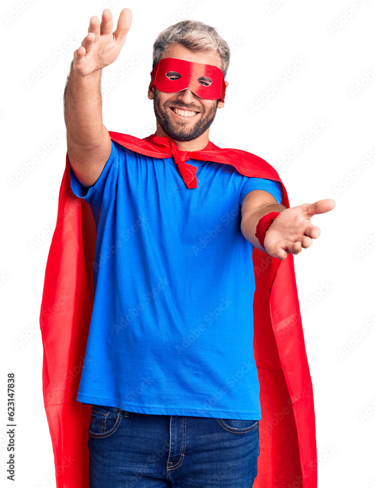 Poster young blond man wearing super hero custome looking at the camera smiling with open arms for hug. che