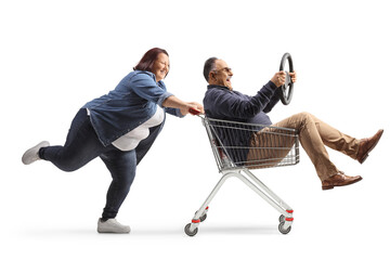 Full length profile shot of a woman pushing a mature man with a steering wheel inside a shopping...