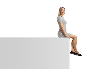 Casual young woman sitting on a white wall