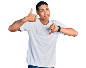 Young hispanic man wearing casual white t shirt doing thumbs up and down, disagreement and agreement expression. crazy conflict