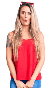 Young beautiful blonde woman wearing sleeveless t-shirt and sunglasses making fish face with lips, crazy and comical gesture. funny expression.