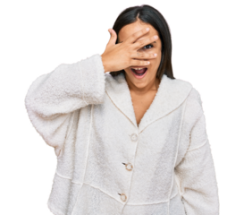 Young brunette woman wearing casual clothes peeking in shock covering face and eyes with hand, looking through fingers with embarrassed expression.