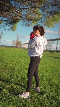 Dedicated female boxer dreesd hoodie warming up arm muscule. Athletic female prepares for boxing workout outdor in park. Female fitness motivation. Fighter warm up body before training. Vertical shoot