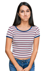 Young hispanic girl wearing casual striped t shirt puffing cheeks with funny face. mouth inflated with air, crazy expression.