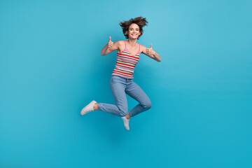 Fototapeta na wymiar Full body portrait of excited carefree lady jumping have good mood demonstrate thumb up isolated on blue color background